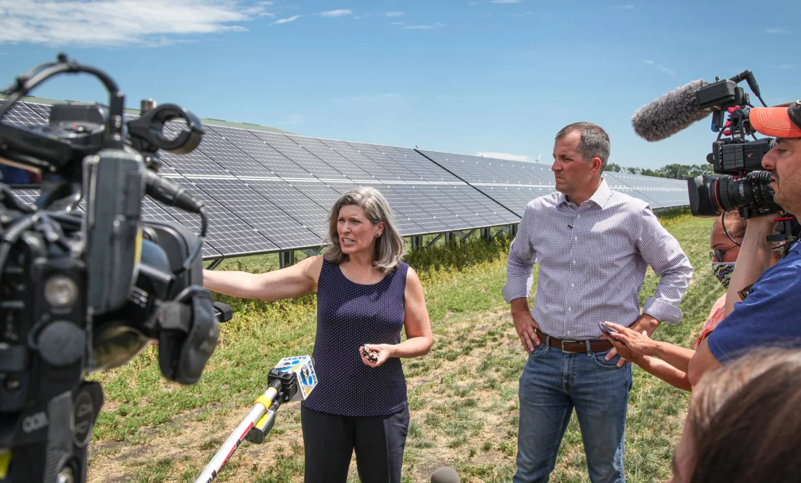 US Senator for Iowa, Joni Ernst, and Iowa Secretary of Agriculture Mike Naig talk to news reporters in front of a row of Blue Horizon Energy solar panels outside Marcus, Iowa.