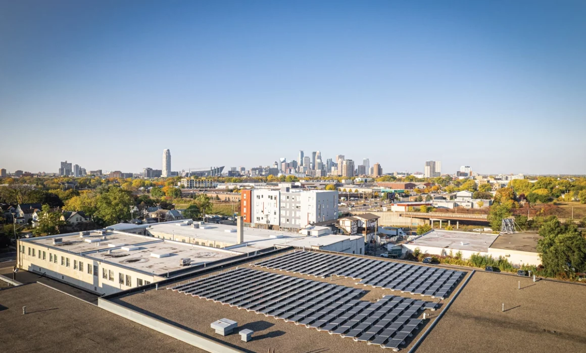 A photo of the downtown Minneapolis skyline on a cloudless morning. In the foreground you see a solar array on the roof of Minnetonka Moccasins' headquarters.
